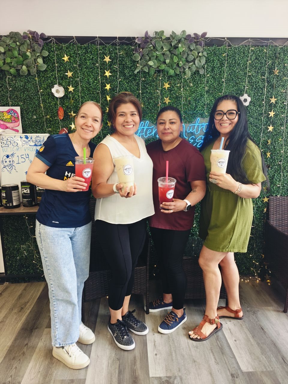 Four customers holding Lifters drinks in front of the green wall